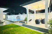 4 Bedroom House for Sale at Rattanakorn Village 18: Backyard with lawn, illuminated pool, and covered outdoor living area.