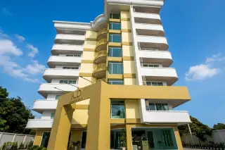 AD Condominium outdoor swimming pool with lounge chairs and the multi-story building facade under a cloudy sky.