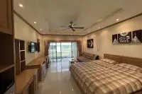 Studio Condo for Sale at Baan Suan Lalana warmly lit studio with king bed, ceiling fan, wooden shelving unit, and balcony sliding doors