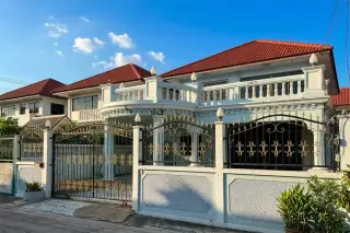 Rungrueang Village, exterior view of a house with a red-tiled roof, light blue balcony, and black wrought iron fence.