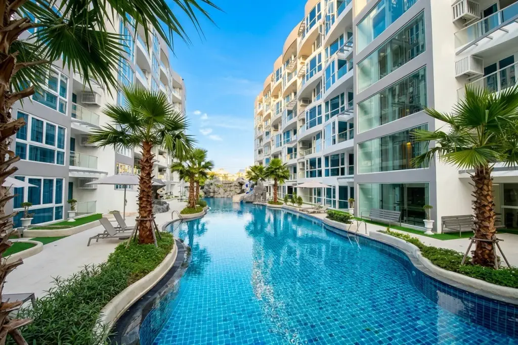 Grand Avenue Residence large swimming pool with water slide, rock waterfall, and palm trees surrounded by condo buildings.