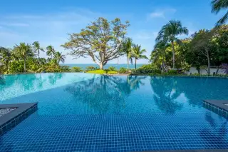 The Cove Pattaya infinity pool with blue mosaic tiles, overlooking the ocean and palm trees.