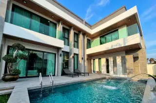 Impress House Village modern exterior at dusk with illuminated trees, covered carport, and a balcony.