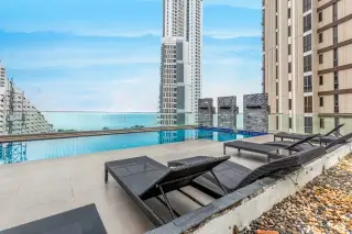Serenity Wongamat rooftop swimming pool with lounge chairs, glass railing, and ocean views.