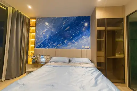 1 Bedroom Condo for Sale & Rent at Arom Wongamat king bed with blue abstract headboard mural, gold backlit shelves, and built-in wardrobe