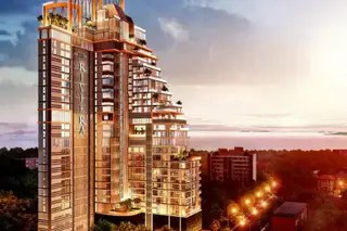 The Riviera Malibu modern high-rise building at dusk, illuminated, with a cityscape and ocean in the background.