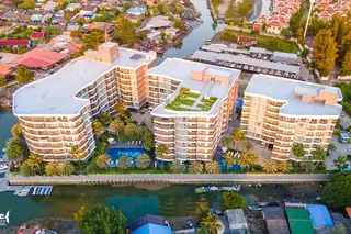 Whale Marina buildings with rooftop gardens, swimming pool, palm trees, and canal with boats.