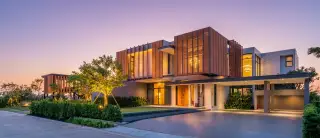 The Prospect modern luxury condo building exterior at dusk, with a large driveway, landscaping, and illuminated interiors.