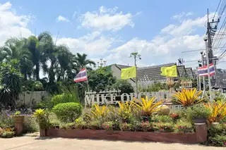 Mike Orchid Villas 2 entrance sign with tropical landscaping, palm trees, and Thai flags under a blue sky.