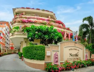 Nordic Residence entrance with colorful flowering balconies, lush greenery, and a 'Welcome to Nordic Residence' sign.