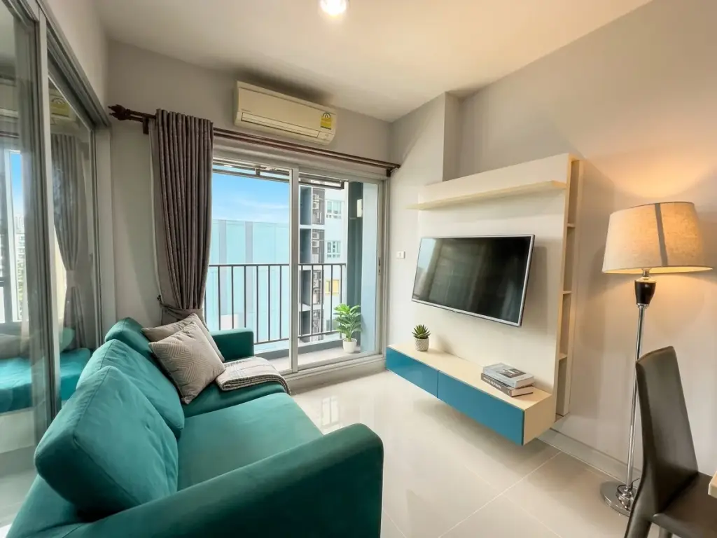 1 Bedroom Condo for Sale at Centric Sea living room with teal sofa, mounted TV, and balcony view