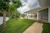 4 Bedroom House for Sale in Nong Prue showing a side view of the covered patio, green lawn, and winding path.