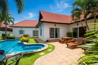 Nirvana Pool Villa 1 exterior with a blue swimming pool, green lawn, tiled patio, and white house with red roof.