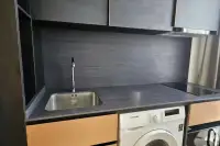 1 Bedroom Condo for Rent at EDGE Central Pattaya dark kitchen with induction hob, sink, overhead cabinets, and washing machine