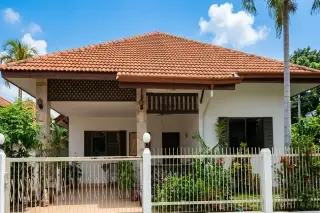 Noen Plub Wan Village white house with brown tiled roof, front fence, and lush green garden in Pattaya, Thailand.