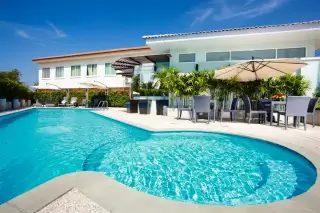Sansuk Town large outdoor swimming pool with lounge chairs, dining sets, and a building under a clear blue sky.