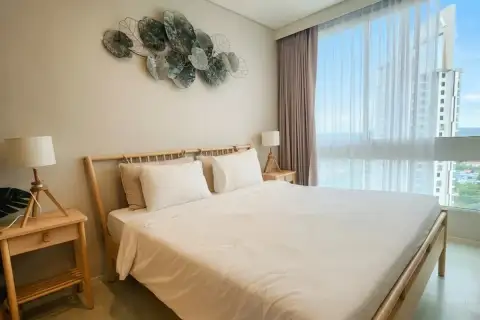 1 Bedroom Condo for Sale at Veranda Residence Pattaya sunlit bedroom with wooden bed frame white bedding and sea view window