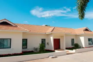 Maprachan 1 single-story condo exterior with cream walls, terracotta roof, red double door, and landscaped garden.