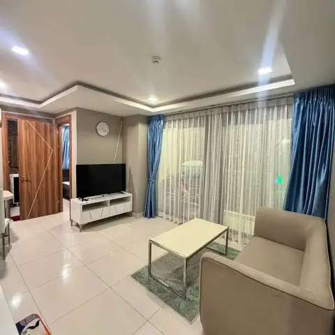 2 Bedroom Condo for Rent at Arcadia Beach Resort living room with sofa, TV stand, and sheer curtains leading to balcony