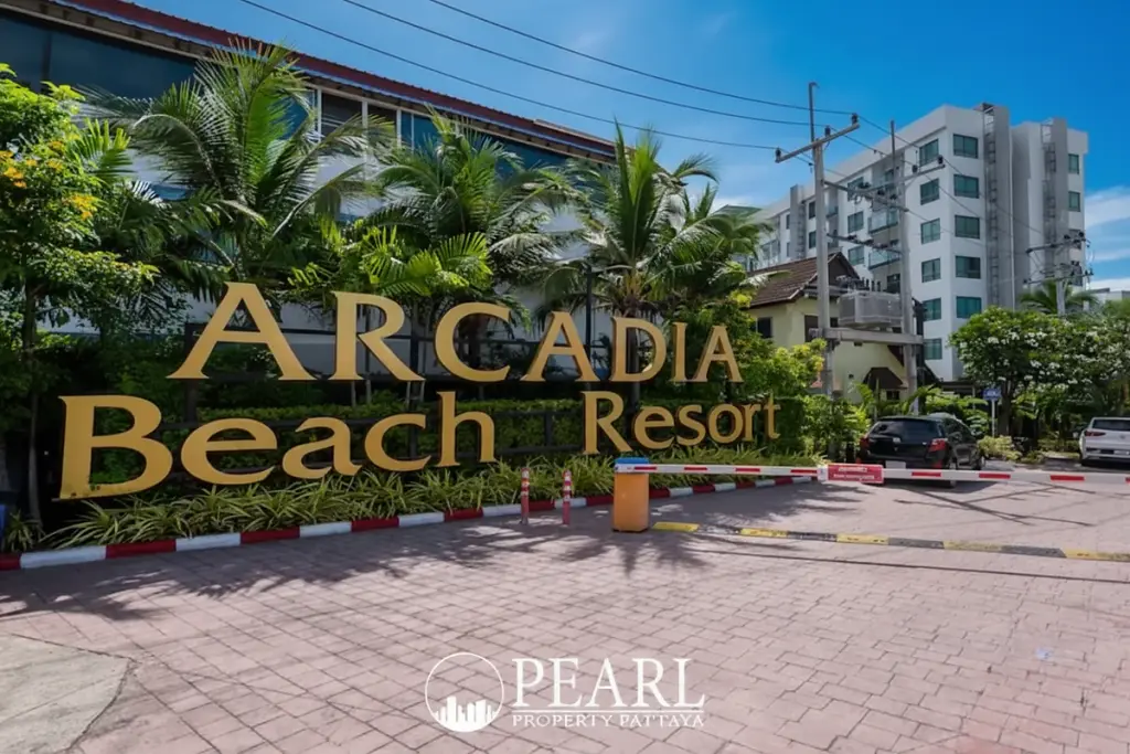 Arcadia Beach Resort entrance sign with golden letters, surrounded by tropical plants and resort buildings.