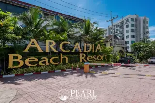 Arcadia Beach Resort entrance sign with golden letters, surrounded by tropical plants and resort buildings.