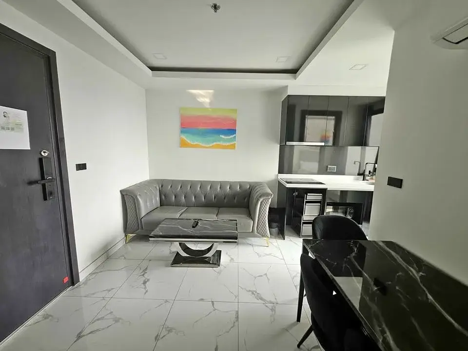 2 Bedroom Condo for Sale at Arcadia Millennium Tower living room with gray tufted sofa, marble coffee table, and open kitchen