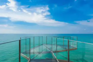 Arom Jomtien glass-bottomed skywalk extending over the ocean with a person in a hat.