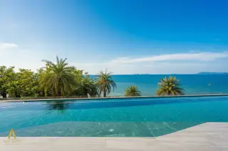 ASONGKHAI Infinity pool with clear blue water and ocean view, palm trees, and distant islands at sunset.
