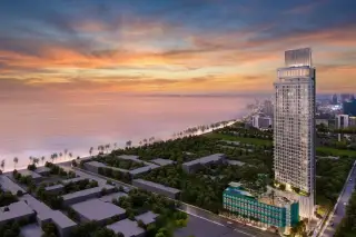 Tait Pattaya: Tall modern condo building with illuminated windows against a twilight sky, with green trees in the foreground.