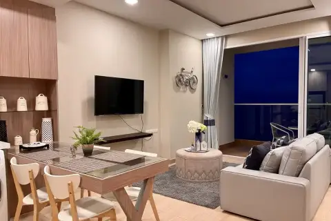 1 Bedroom Condo for Sale at Cetus Beachfront dining and living area with glass-top table, gray sofa, wall TV, and night sea view balcony