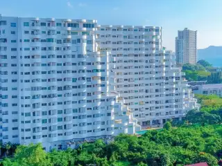 Sunset Heights Condominium: High-angle view of the building, two outdoor pools, green trees, and the blue ocean with a beach.