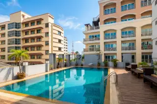 Pattaya Beach Condo outdoor swimming pool with surrounding tile deck and potted plants, buildings in the background.