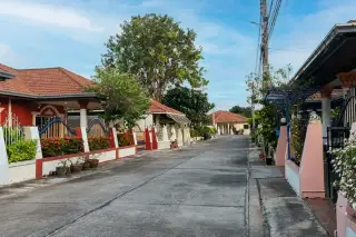 Eakmongkol Chaiyapruek1 exterior with yellow walls, green lawn, palm trees, and a covered entrance with white columns.