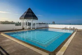 Thien Tong Condotel rooftop swimming pool with a black gazebo, white lounge chairs, and distant ocean view under a clear sky.