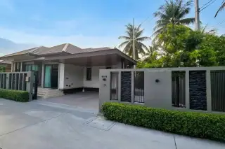 Amarin House 2 front facade with covered carport, decorative gate, manicured hedges, and tropical palm trees