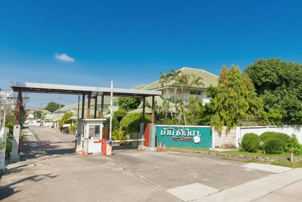 Baan Chalita 1 main entrance gate with security booth, barrier arms, and a green welcome sign with Thai script.