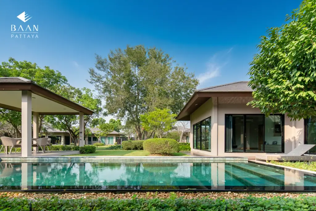 Baan Pattaya 5 outdoor swimming pool with a modern house, covered patio, and people enjoying the garden.