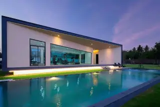 Baan Pattaya 6 exterior view of a modern house with a green lawn and large sliding glass doors.