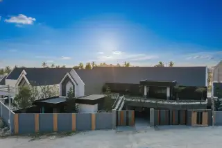 Baan Mae Grand aerial view of modern condo complex with gabled roofs, dark facades, and a large entrance at sunset.