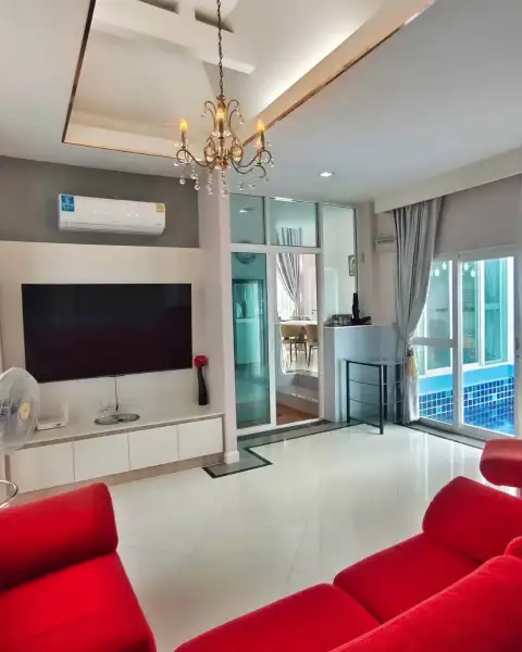 3 Bedroom House for Rent in Bang Sare living room with red sofas, mounted TV, and pool view