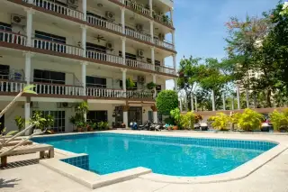 Holiday Condo View of a multi-story building with balconies overlooking a blue swimming pool and tropical landscaping.