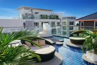 C-View Boutique and Residence rooftop pool with blue tiles, round daybeds, and palm trees, overlooking city buildings.