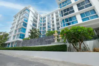 Serenity Wongamat condo building exterior with modern white facade, blue windows, and lush green landscaping.