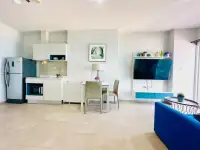 1 Bedroom Condo for Rent at Centric Sea open-plan kitchen, dining table, and living area with blue sofa and mounted TV