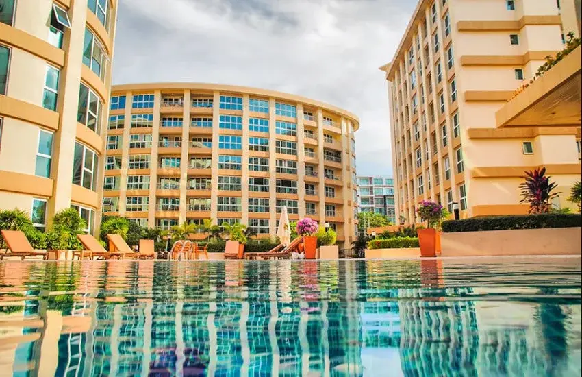 City Garden Pattaya swimming pool with lounge chairs, umbrellas, and apartment buildings in the background.