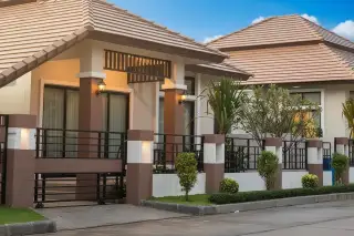 Classic Garden Home exterior view of two modern homes with brown tiled roofs, illuminated facades, and a decorative fence at dusk.