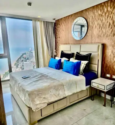 1 Bedroom Condo for Rent at Copacabana Beach Jomtien bedroom with king bed, blue accent pillows, and ocean view window