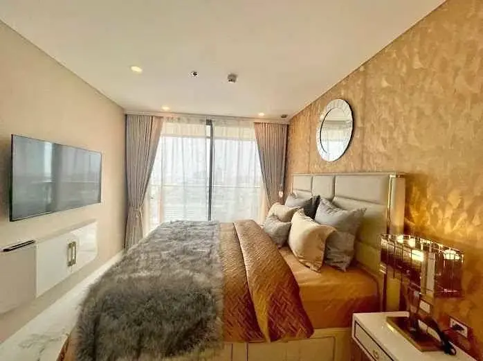 1 Bedroom Condo for Sale at Copacabana Beach Jomtien bedroom with gold accent wall, round mirror, and wall-mounted TV