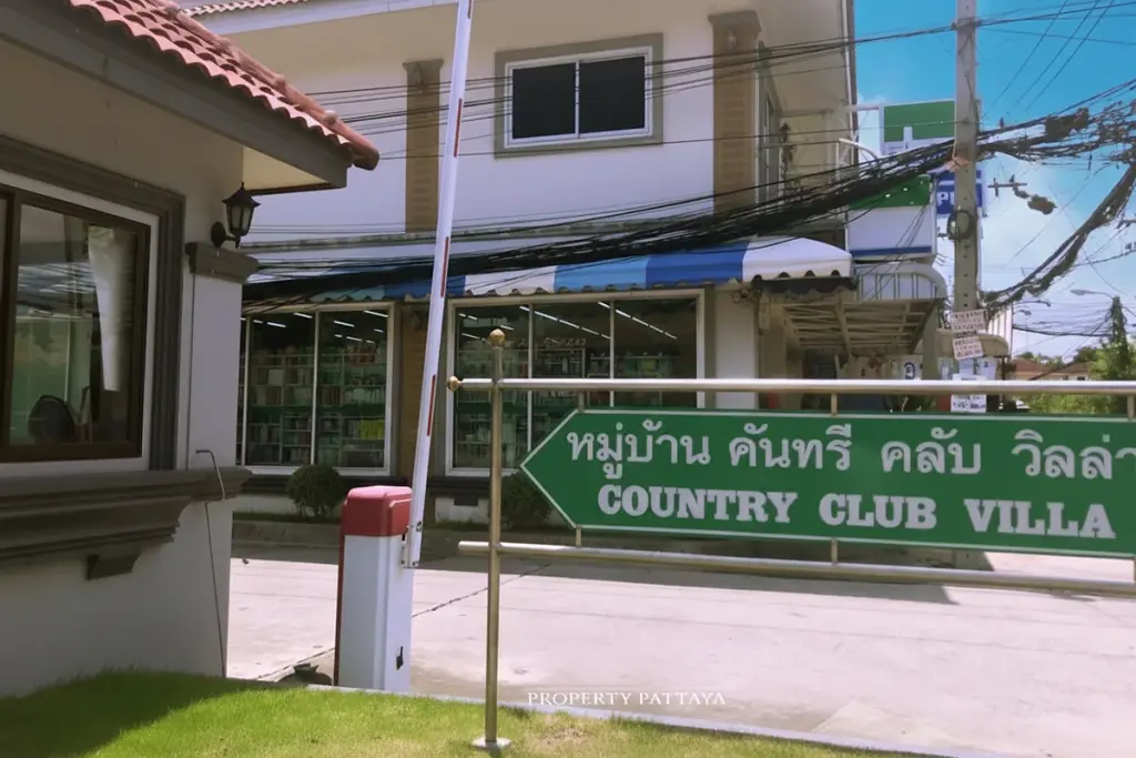 Country Club Villa entrance gate with a green sign and a convenience store in the background.