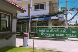 Country Club Villa entrance gate with a green sign and a convenience store in the background.